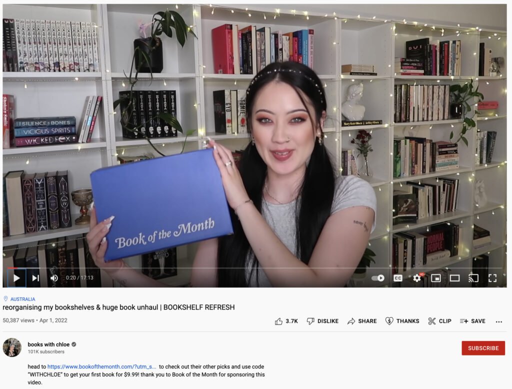 Screenshot of a YouTube video by "books with chloe" that is sponsored by Book of the Month. Chloe is holding up the blue Book of the Month box in front of her bookshelves.